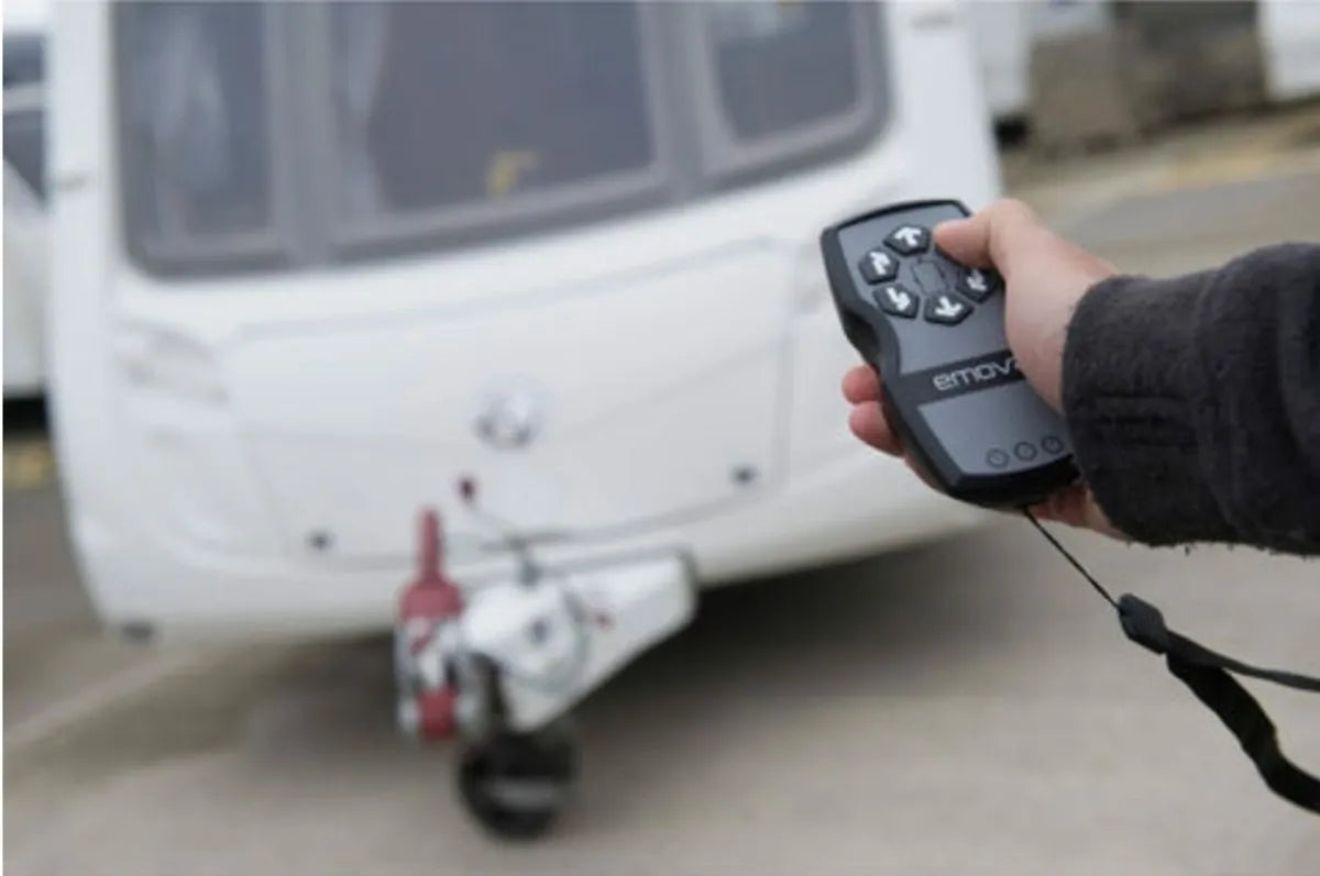 A hand controlling The EM303 caravan mover, is also pointed to a caravan in the distance.